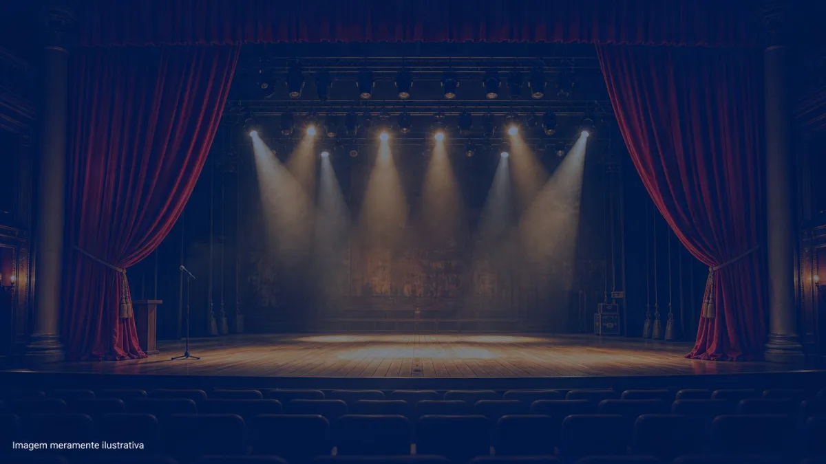 Palco de teatro vazio com cortina vermelha aberta e refletores acesos, imagem meramente ilustrativa