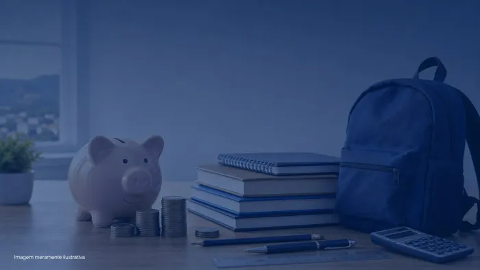 Cofrinho ao lado de livros escolares, caderno e mochila sobre mesa de estudo, imagem meramente ilustrativa