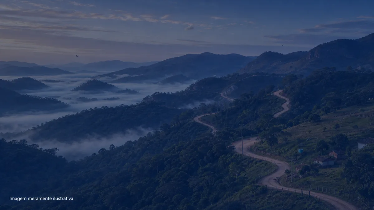 Morros cobertos de mata preservada com estrada de terra serpenteando na neblina, imagem meramente ilustrativa