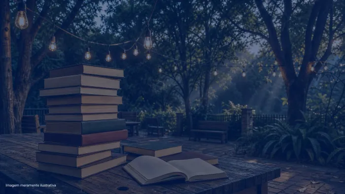 Livros empilhados sobre mesa de madeira em area externa arborizada com lampadas penduradas, imagem meramente ilustrativa