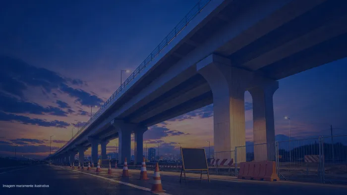 Viaduto urbano visto de angulo baixo ao entardecer com cones de obra na pista, imagem meramente ilustrativa
