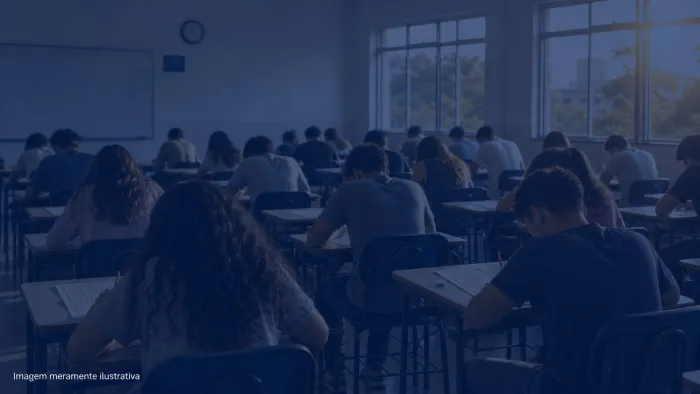 Sala de aula com carteiras enfileiradas e estudantes de costas fazendo prova, imagem meramente ilustrativa