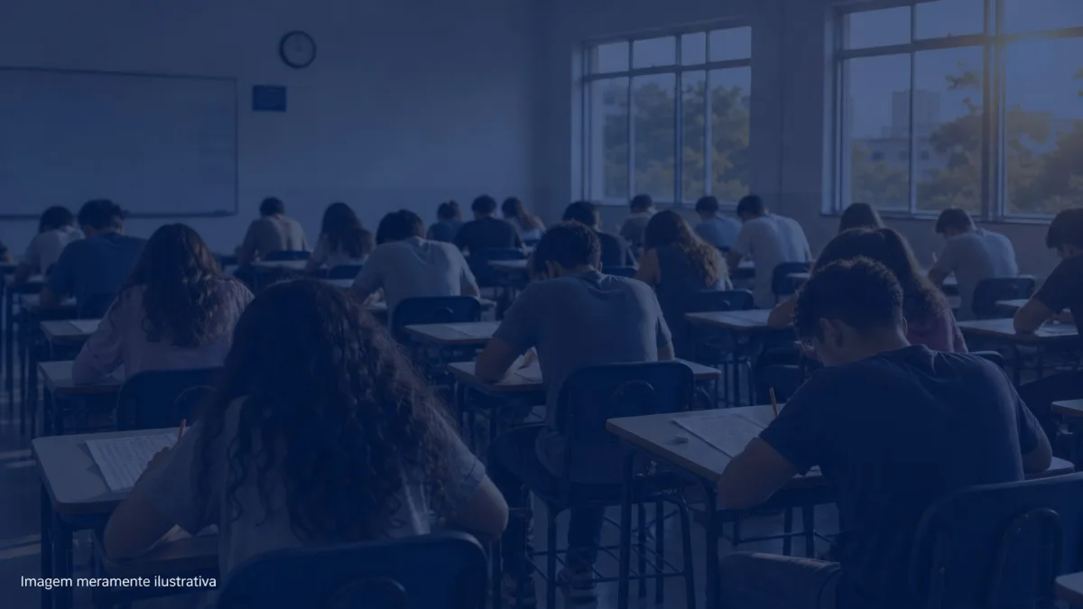 Sala de aula com carteiras enfileiradas e estudantes de costas fazendo prova, imagem meramente ilustrativa