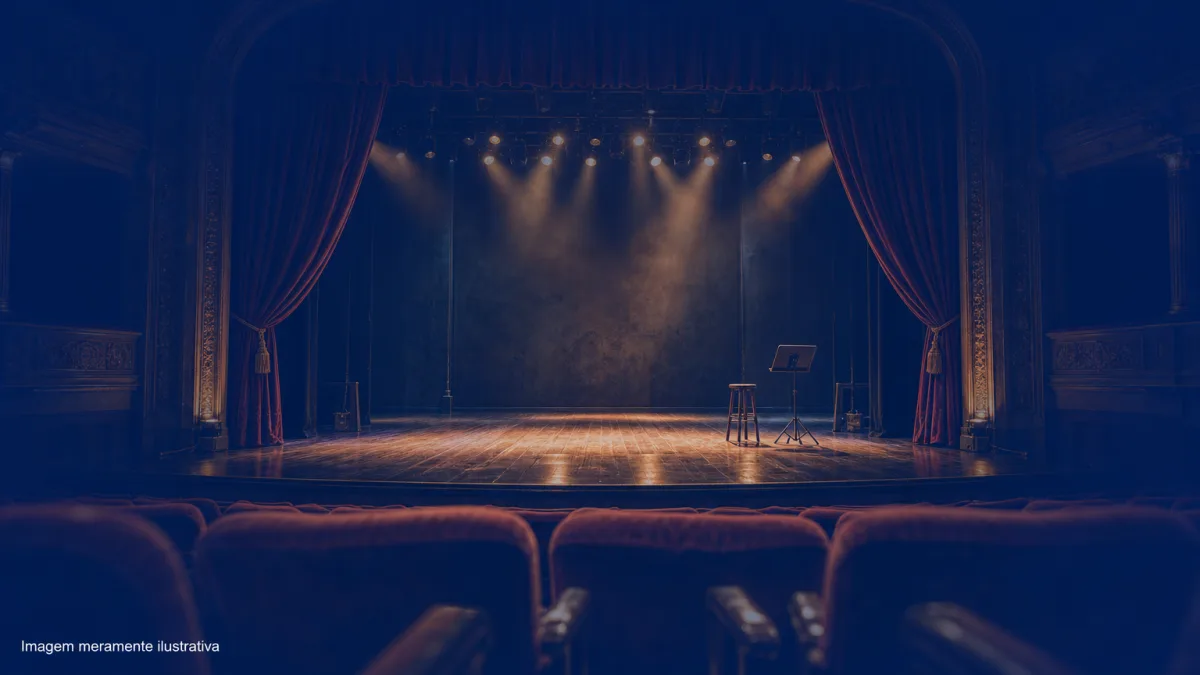 Palco de teatro visto da plateia, com cortina aberta e iluminação cênica, imagem meramente ilustrativa